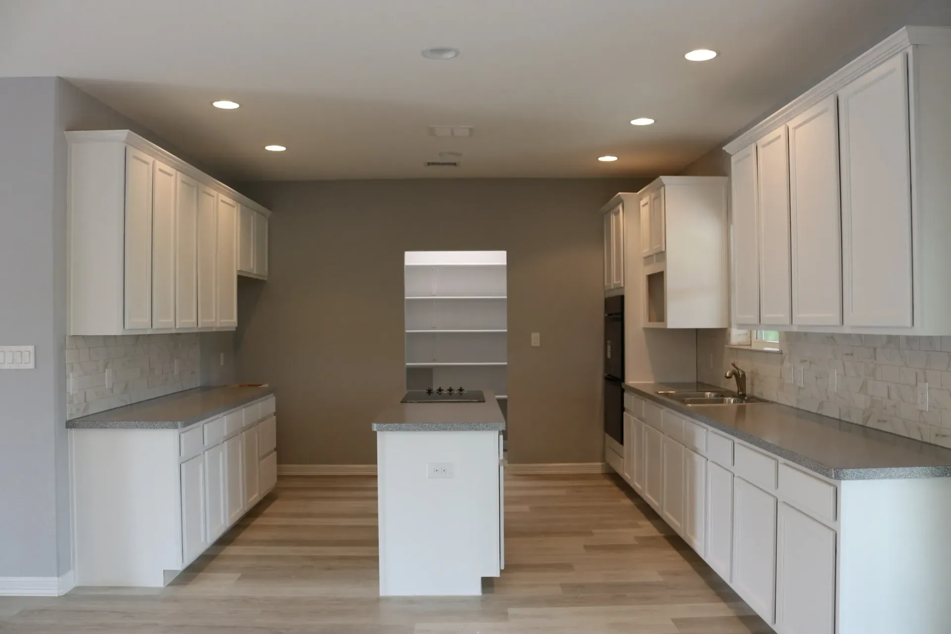 Empty white kitchen with cabinetry, island, and pantry entrance.