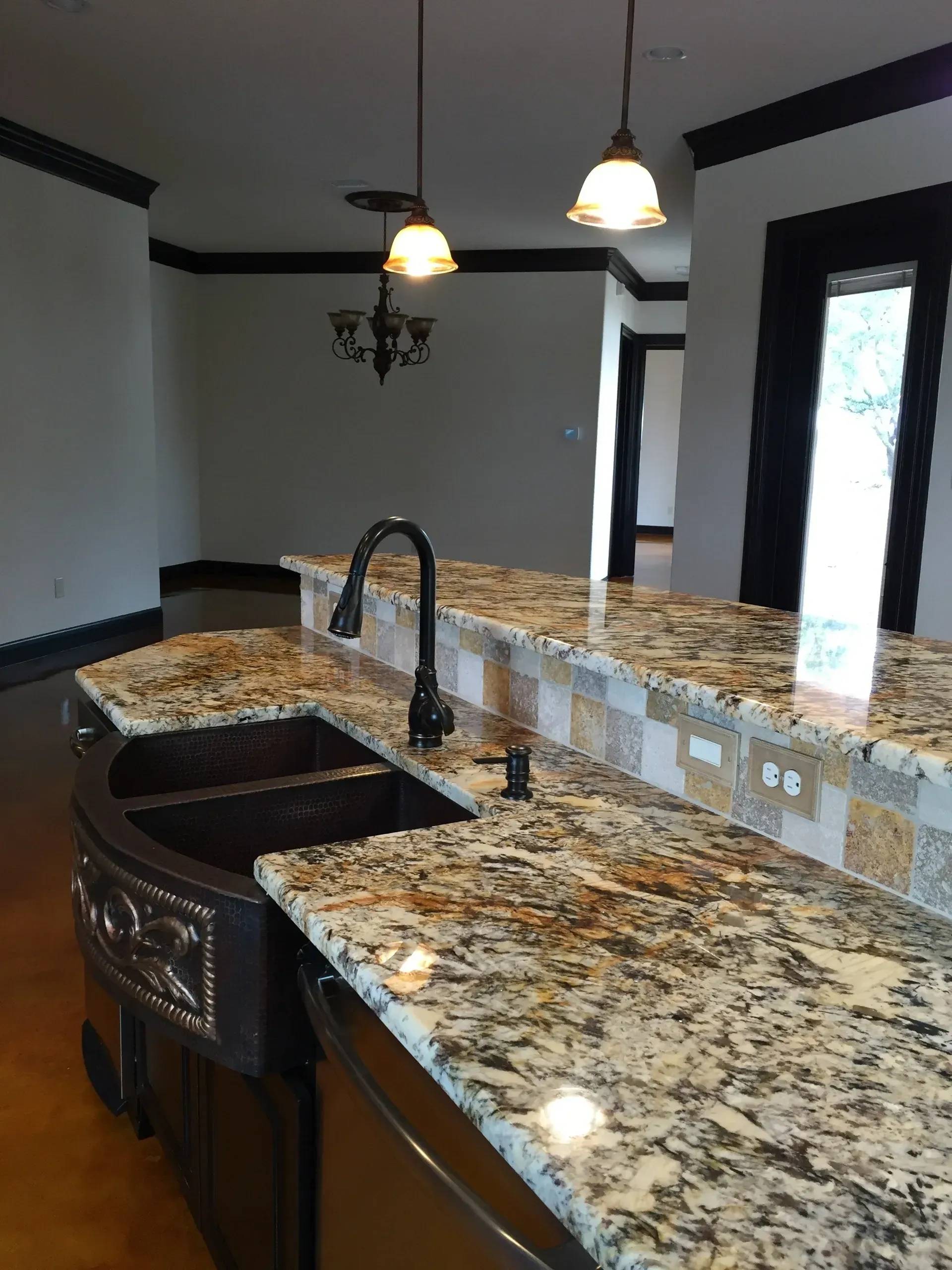 Kitchen island with granite countertop, dark sink and faucet, pendant lights.
