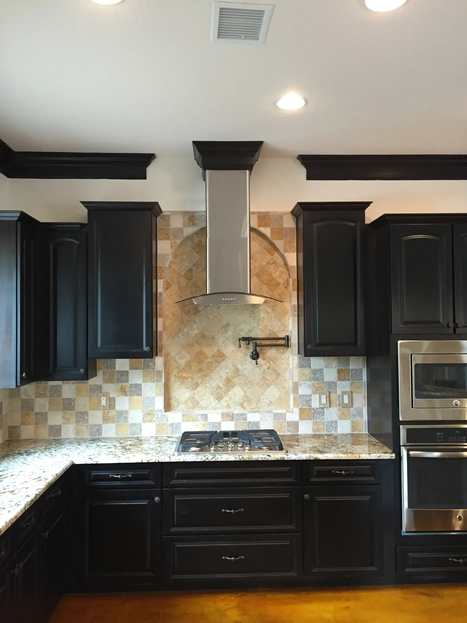 Black kitchen cabinets with a stainless steel range hood, granite countertops, and tile backsplash.