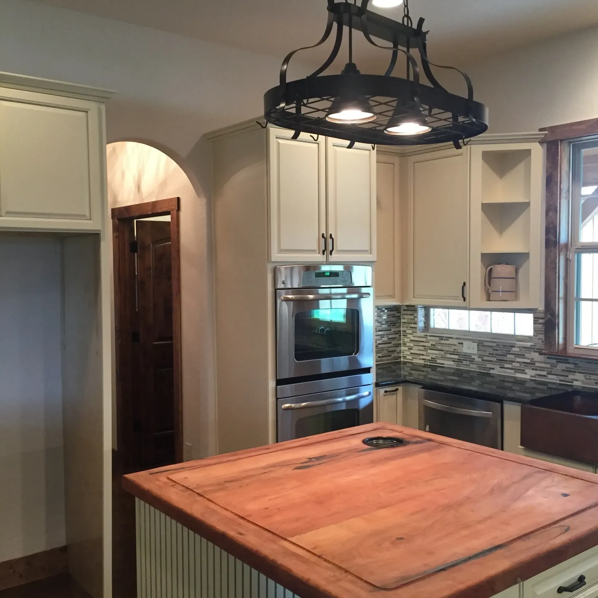 Kitchen with light cabinets, wood island, and a dark, ornate light fixture.