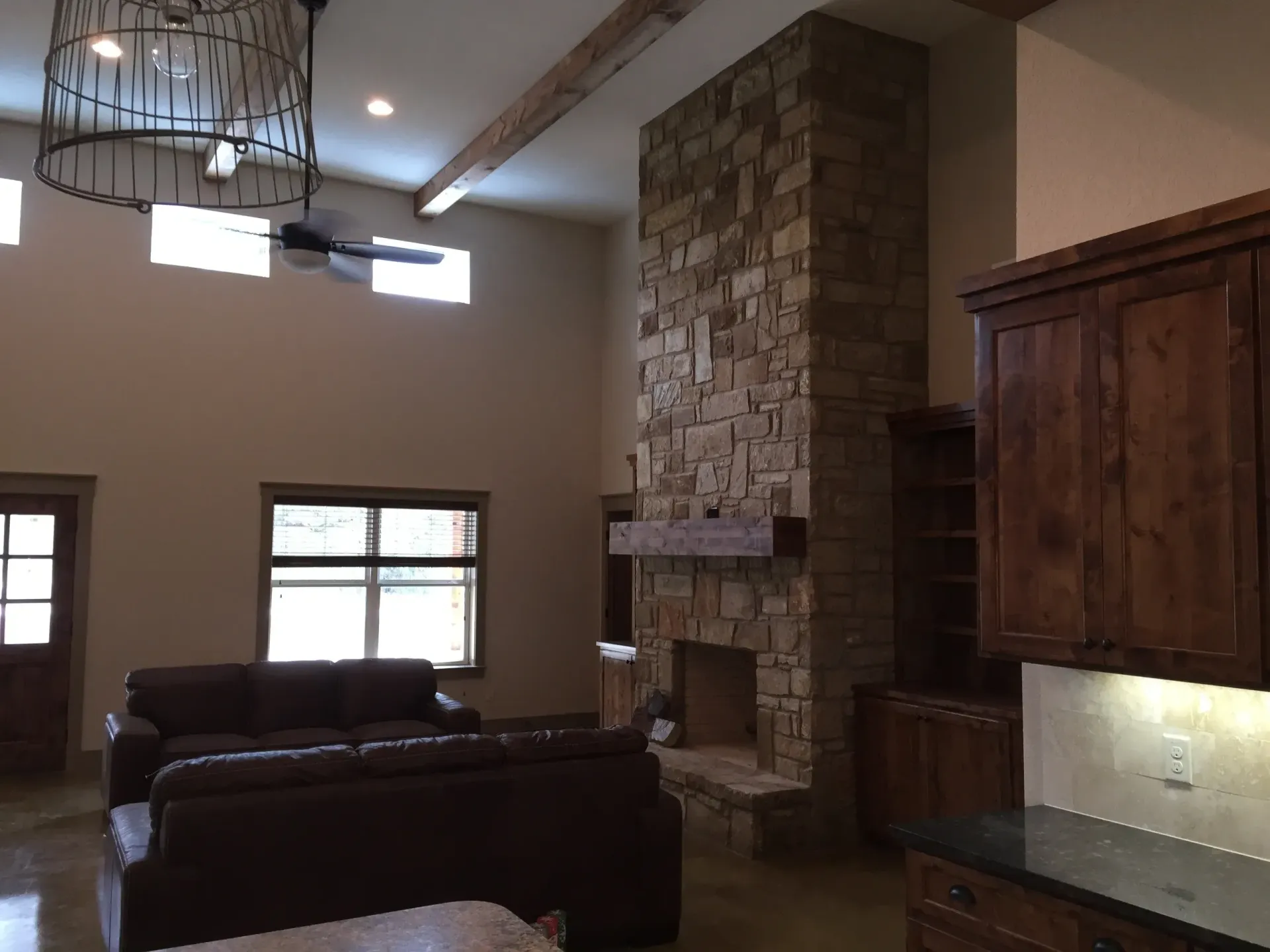Living room with stone fireplace, brown furniture, high ceilings, and exposed wooden beams.