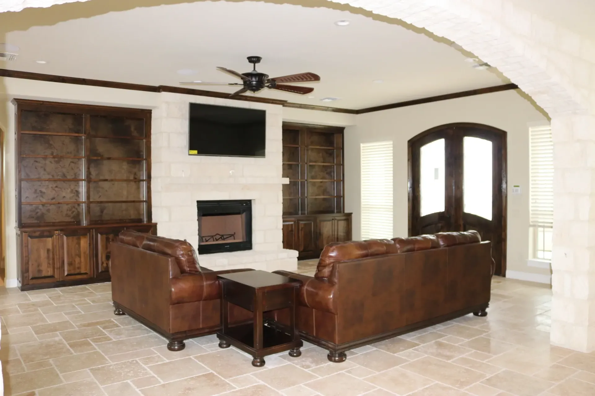 Living room with brown leather furniture, fireplace, built-in shelves, and a dark ceiling fan.