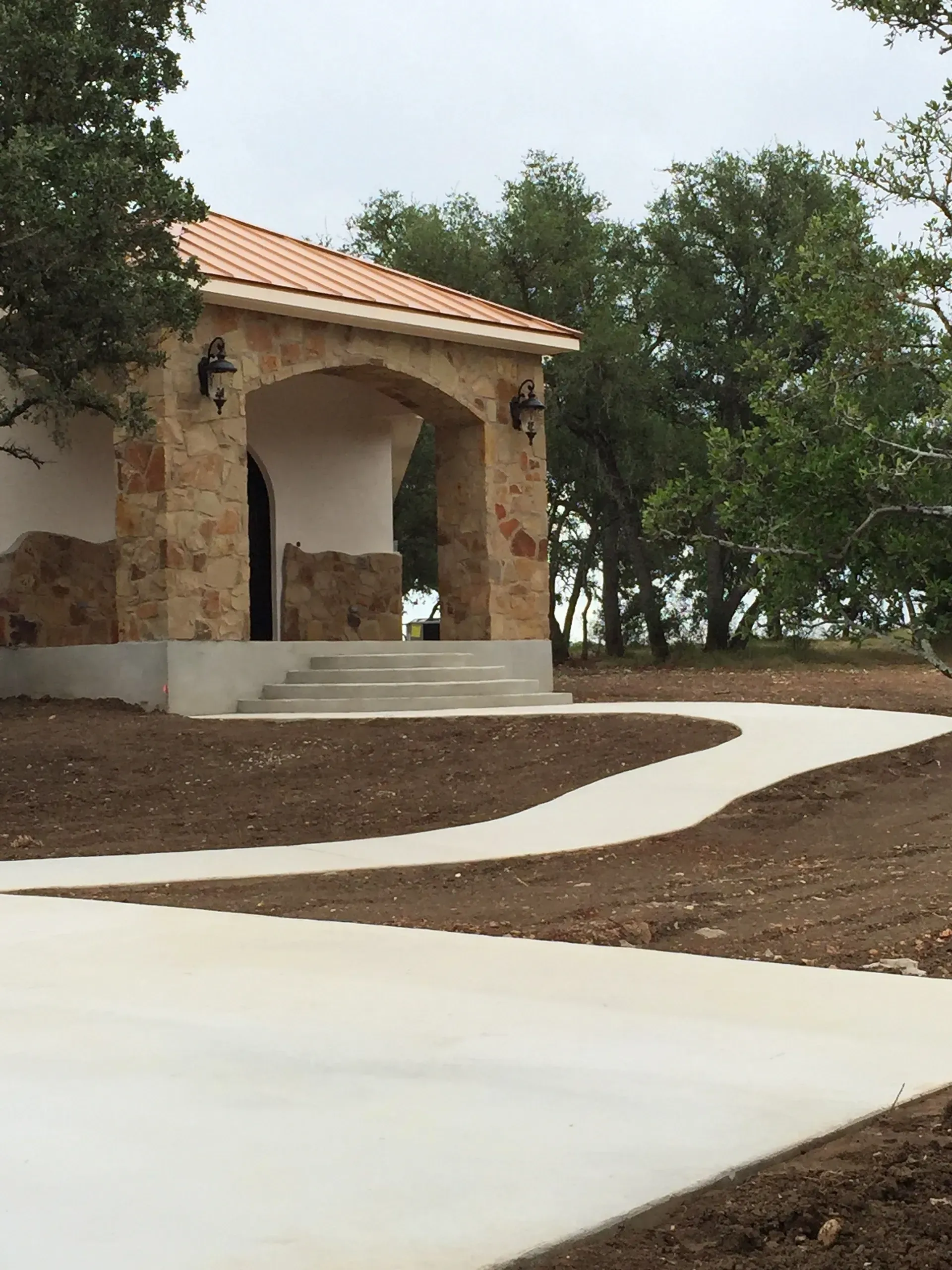 Stone building with arched entrance and curved concrete walkway.