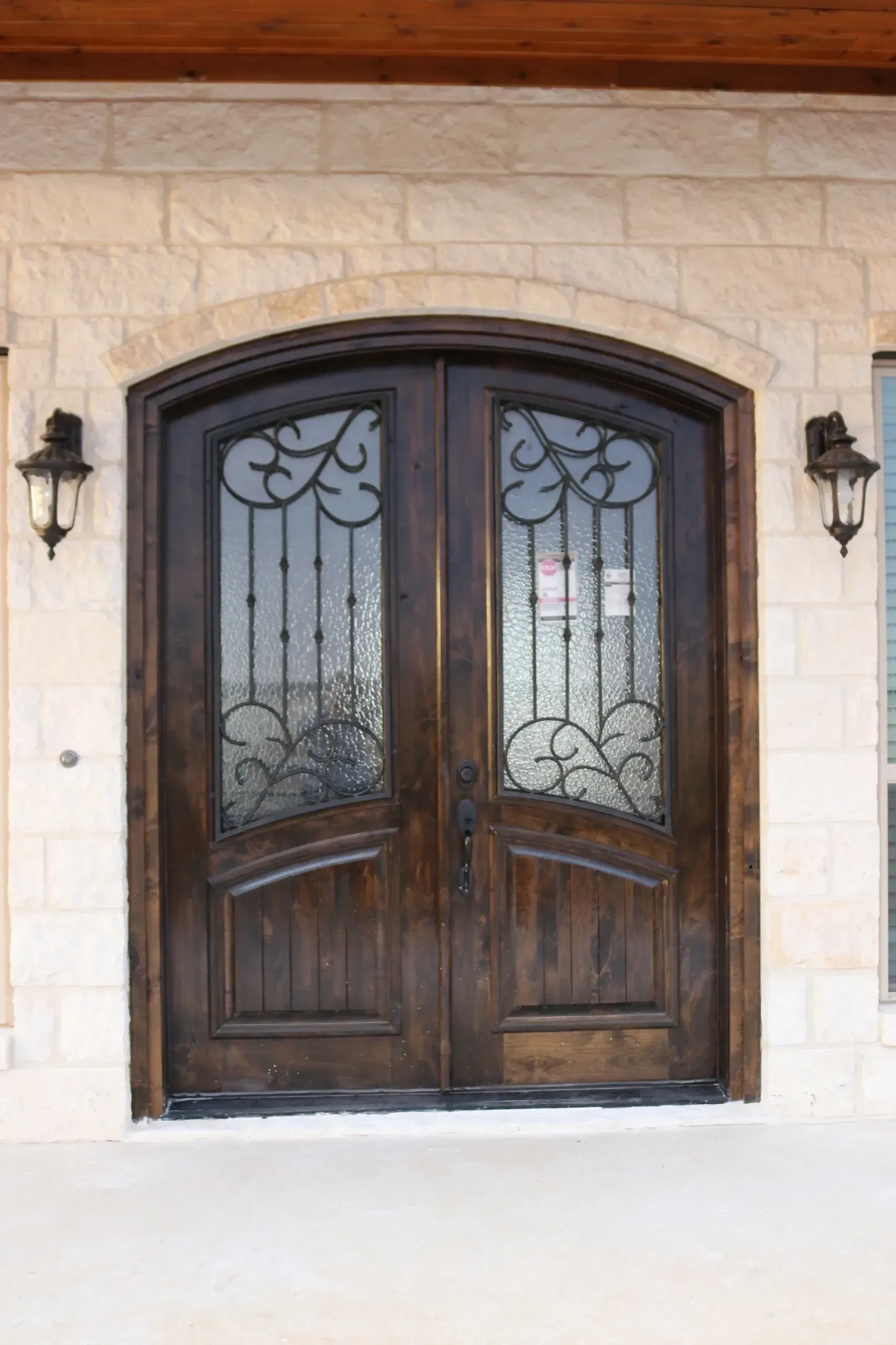 Double wooden front doors with arched top, decorative ironwork, and sidelights.