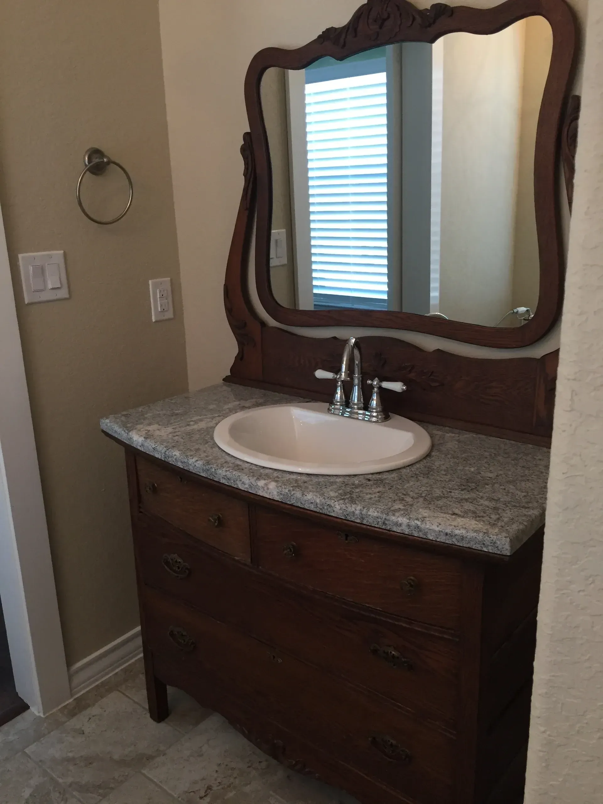 Antique vanity with a dark wood cabinet, granite countertop, oval sink, and ornate mirror.