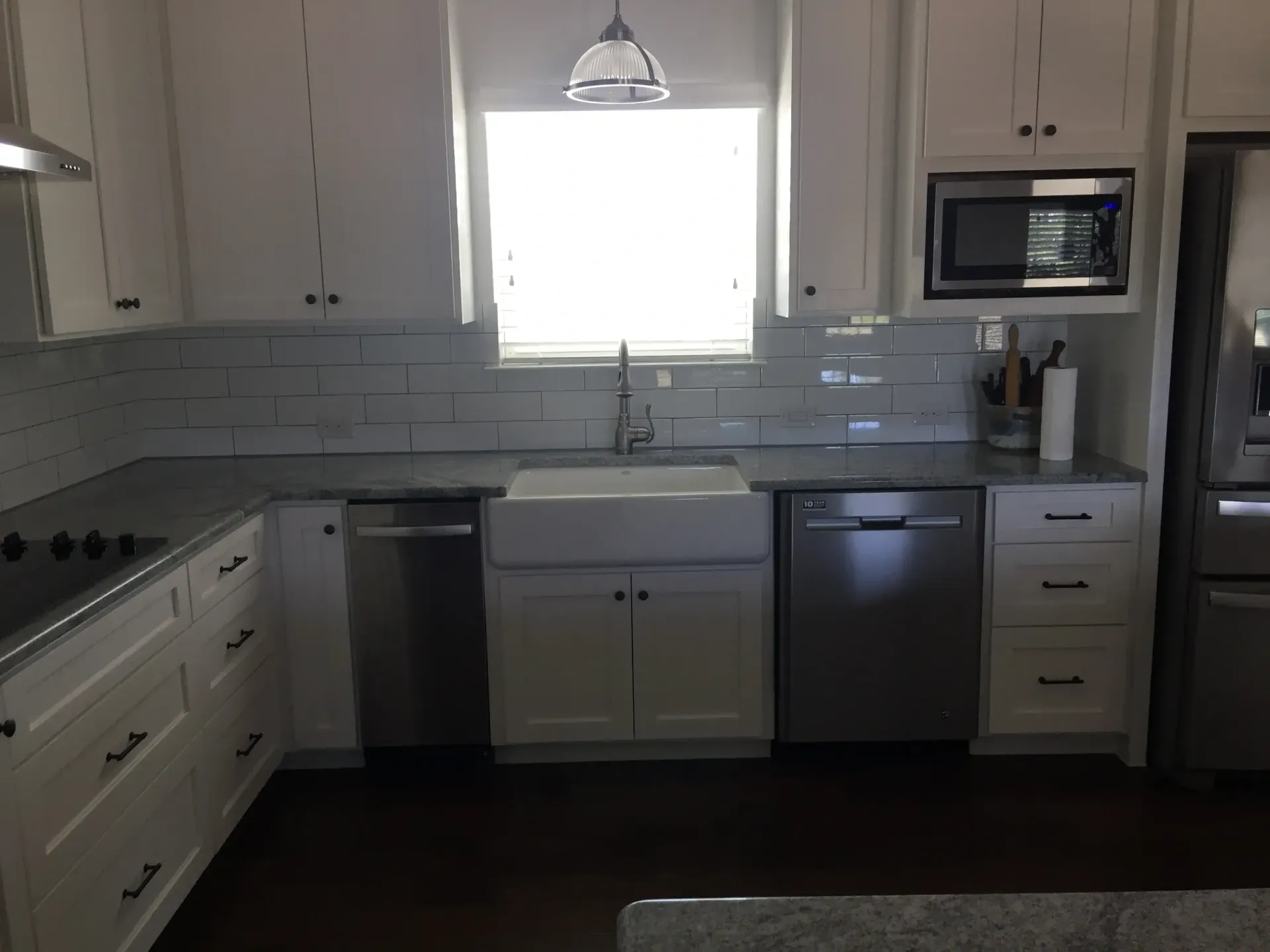 White kitchen with stainless steel appliances, a farmhouse sink, and gray countertops.