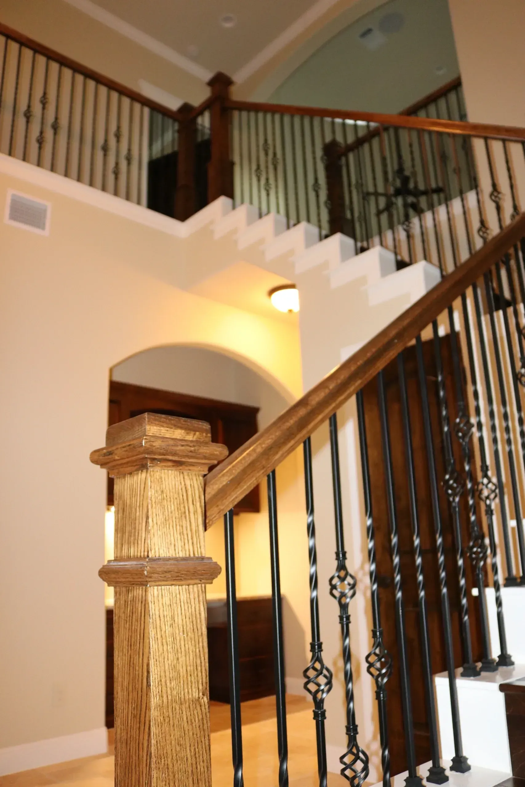 Wooden staircase with black metal balusters and arched entry.