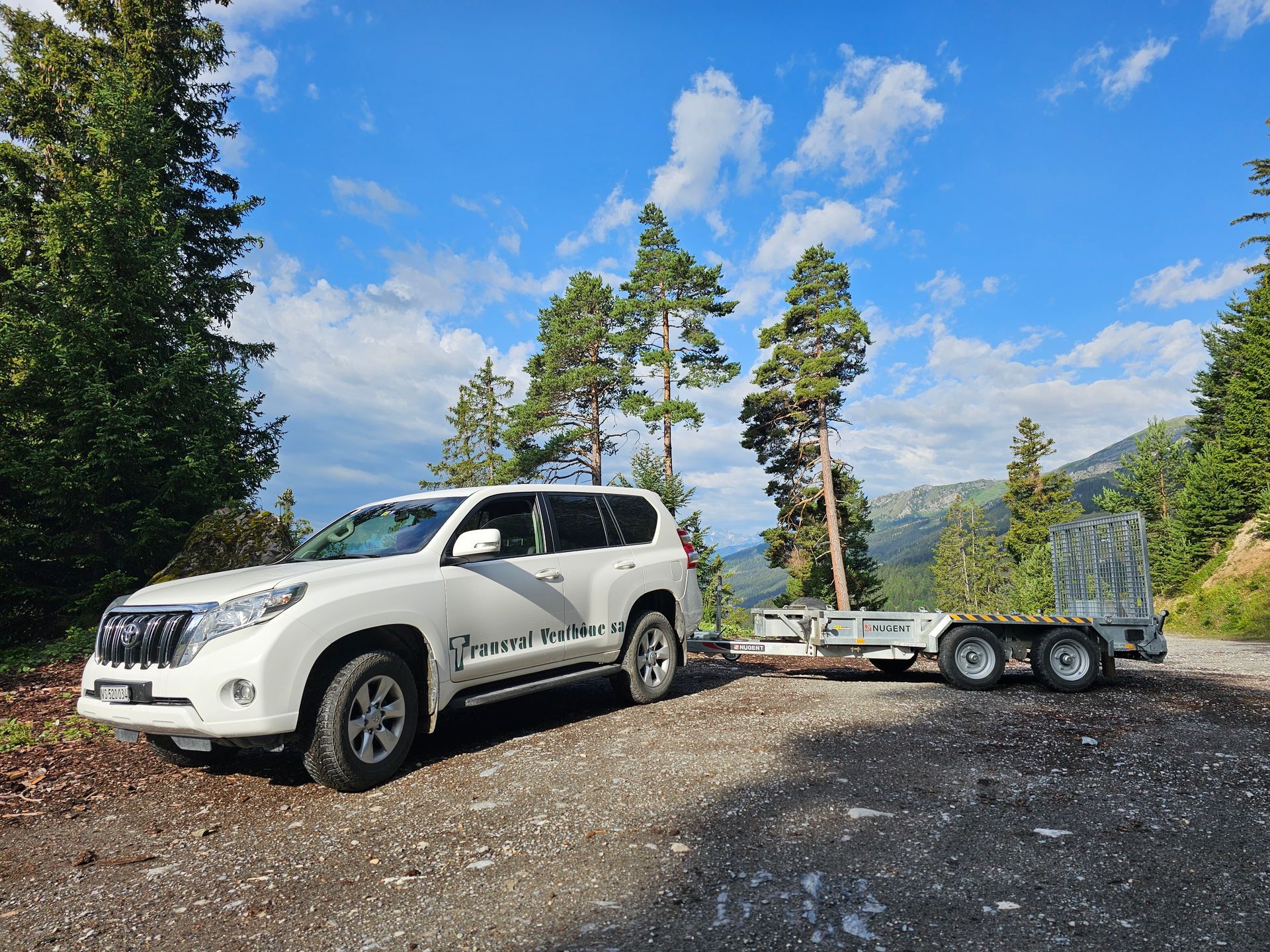 Un SUV blanc est garé à côté d'une remorque sur un chemin de gravier.