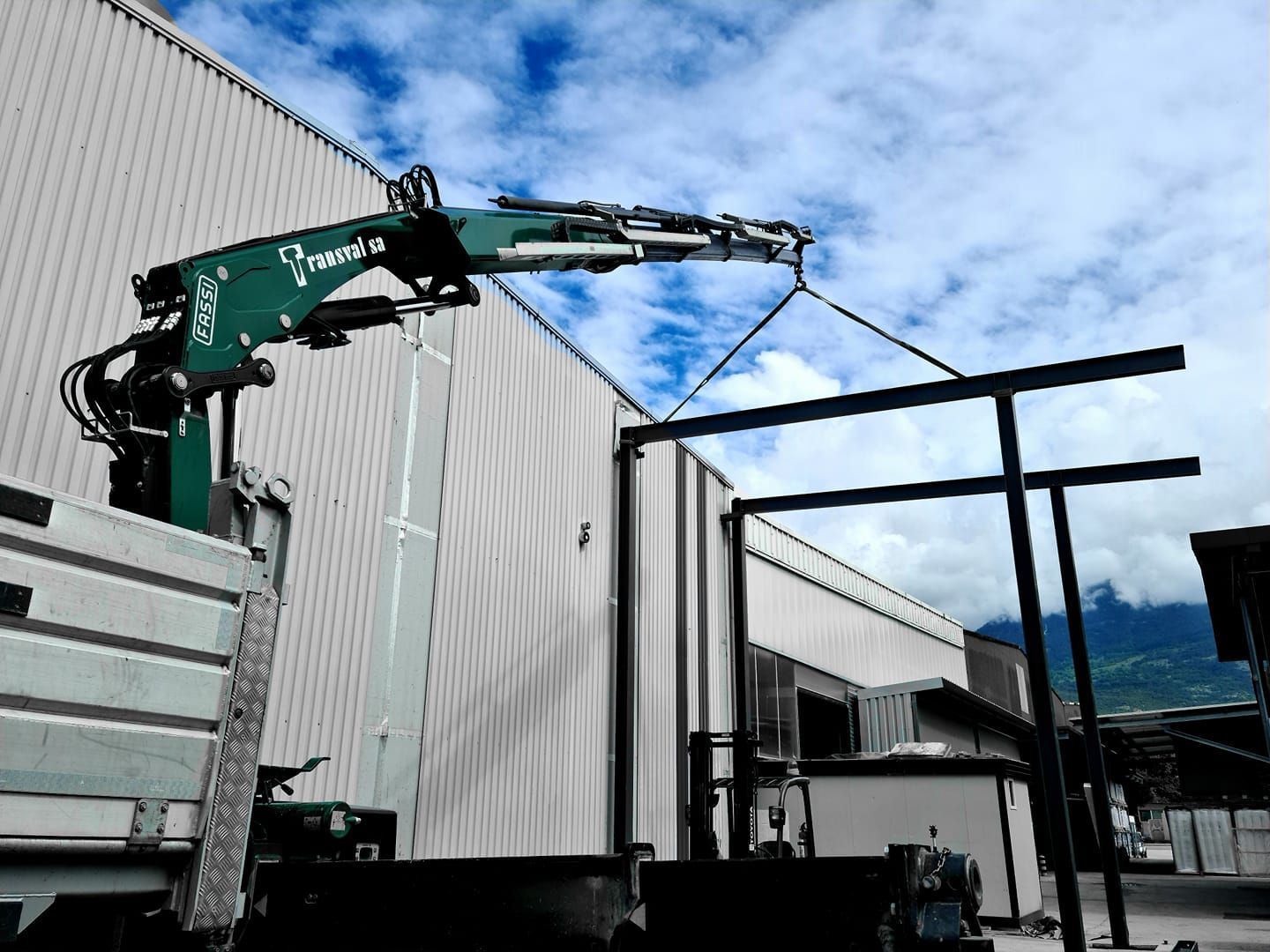 Une grue soulève un morceau de métal devant un bâtiment