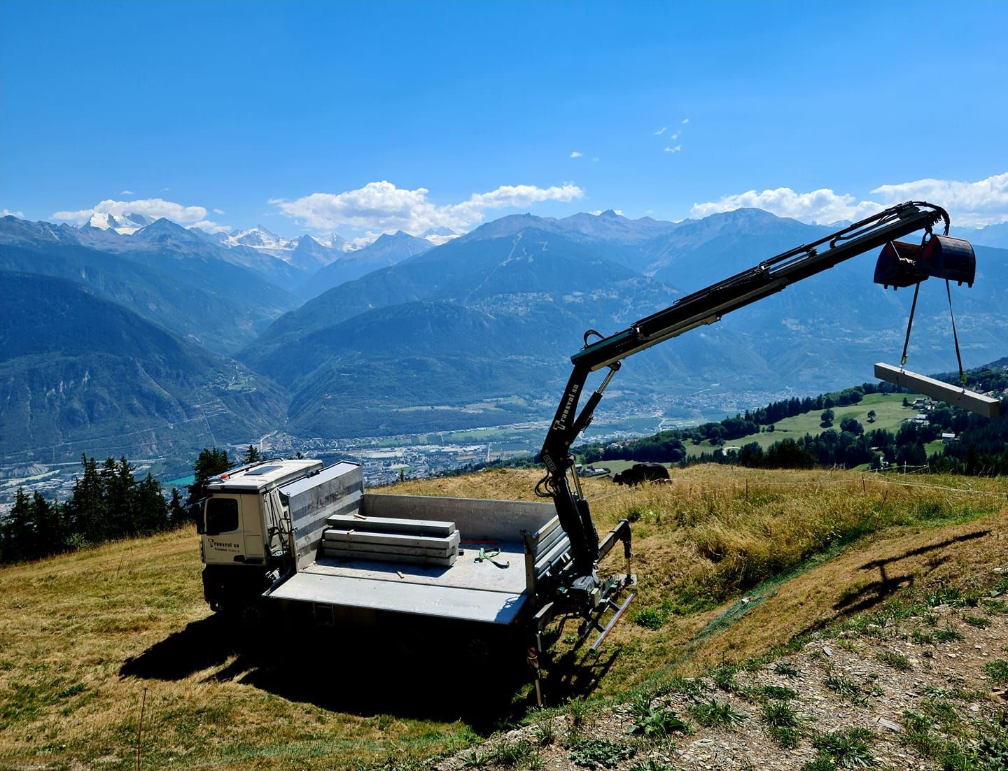 Un camion est garé au sommet d'une colline herbeuse avec des montagnes en arrière-plan.