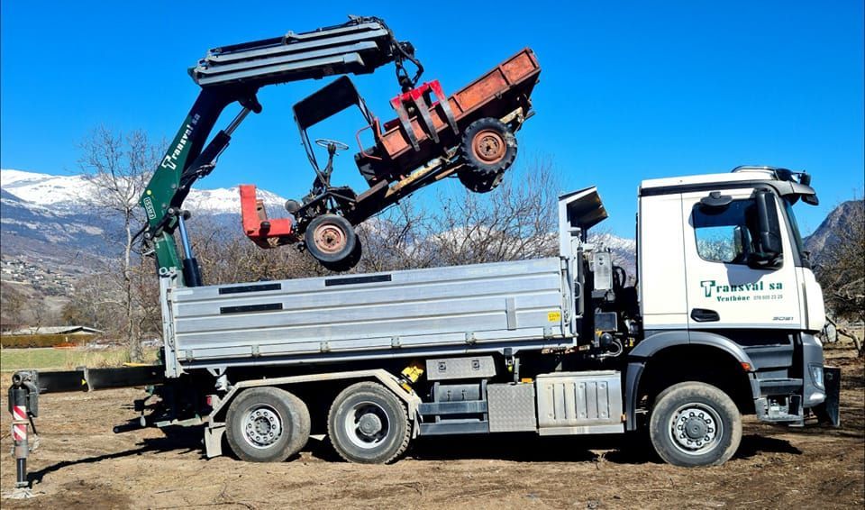 Un camion avec une grue attachée transporte un tracteur.