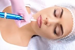 Person undergoing lip blushing; pink-gloved hand holding a tattoo pen; indoors.