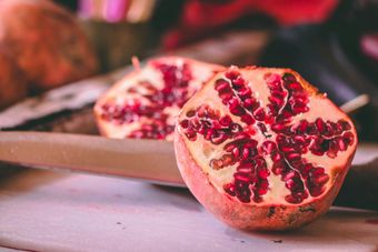 Half of a ripe pomegranate, revealing juicy red seeds, on a wooden board.