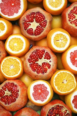 Cut citrus fruits and pomegranates arranged together; oranges, grapefruits, and pomegranates in shades of red and orange.