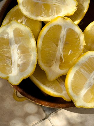 Sliced lemons in a brown bowl, close-up. Yellow fruit, white pith, on a neutral background.