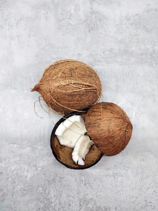Three coconuts on a gray surface, one cracked open with white flesh visible.