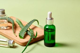 Green glass bottle with dropper next to aloe vera leaves and small bottles on a wooden board.