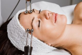 Woman receiving a microcurrent facial treatment. The woman lies on a table, electrodes touch her face.
