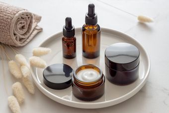 Skincare products arranged on a white tray, including bottles, jars of cream, and a rolled towel.