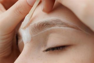 Person having eyebrow waxing done; white wax applied around the eyebrow.