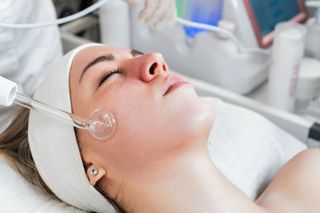 Woman receiving facial treatment with a glass wand on her cheek.