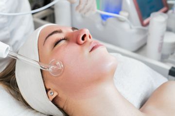 Woman receiving a facial treatment with a handheld high-frequency device at a spa.