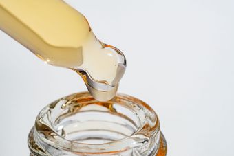 Dropper dispensing yellow liquid into a glass bottle, close-up view.