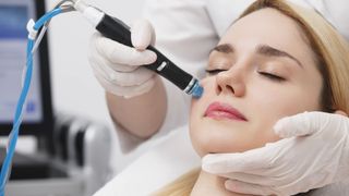 Woman receiving a facial treatment with a handheld device; gloved hands, close-up, clinic setting.