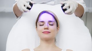 Woman receiving blue light facial treatment with eyes closed at a spa.