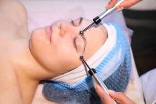 Woman receiving a facial treatment with handheld devices; closed eyes, salon setting.