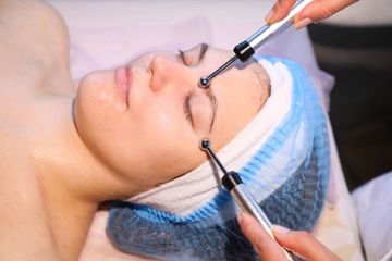Woman undergoing facial treatment with electrical probes in a spa setting.