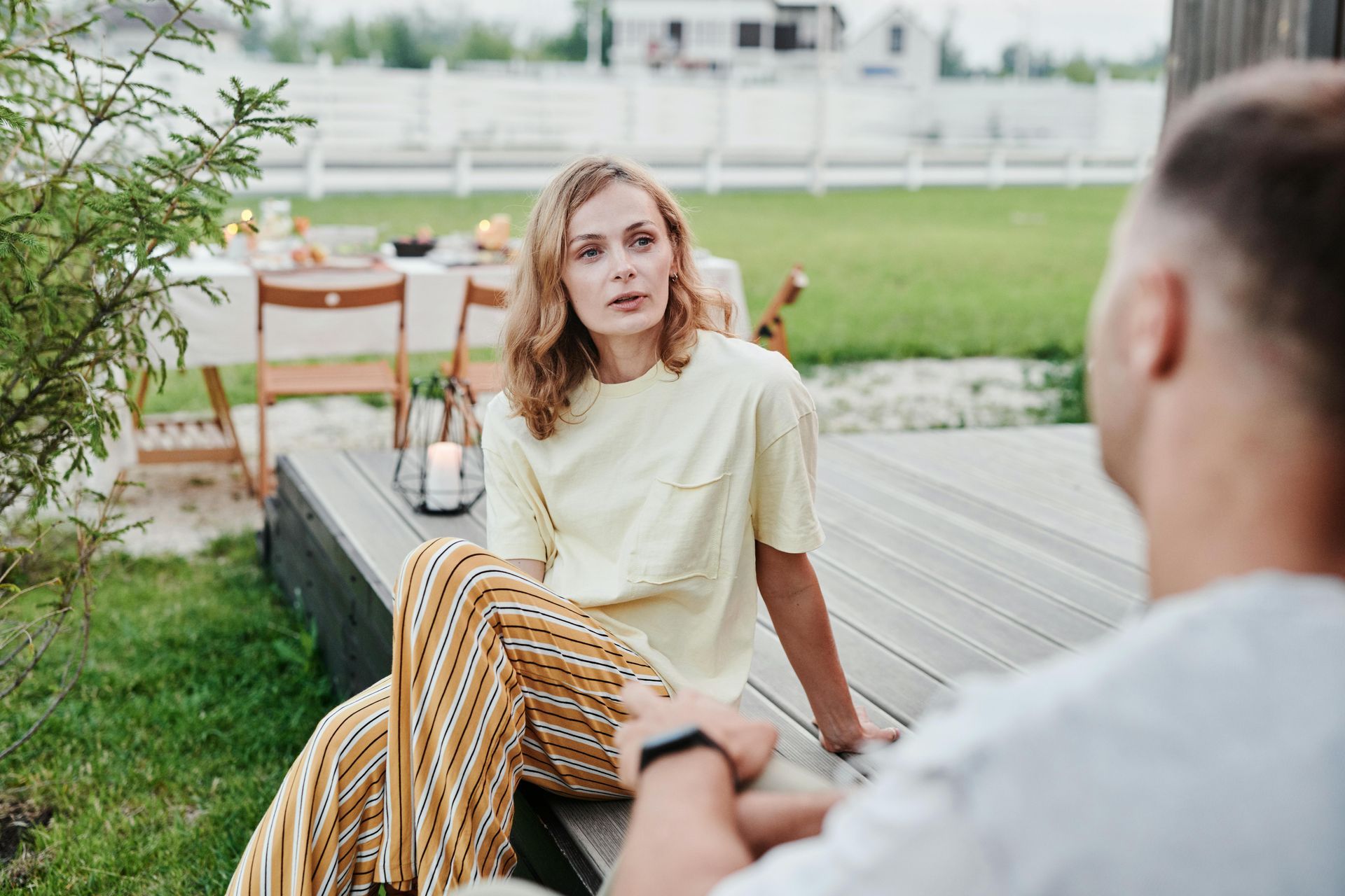 A man and a woman are sitting on a wooden deck talking to each other.