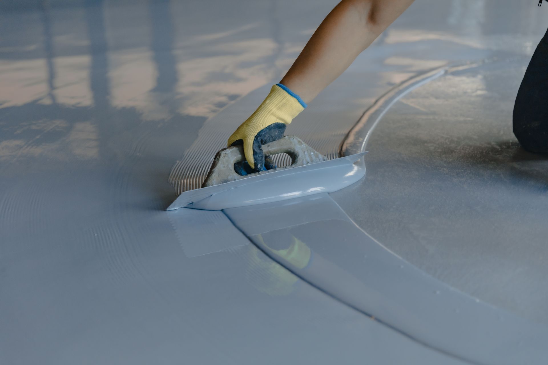 A person is applying a coating to a concrete floor with a trowel.
