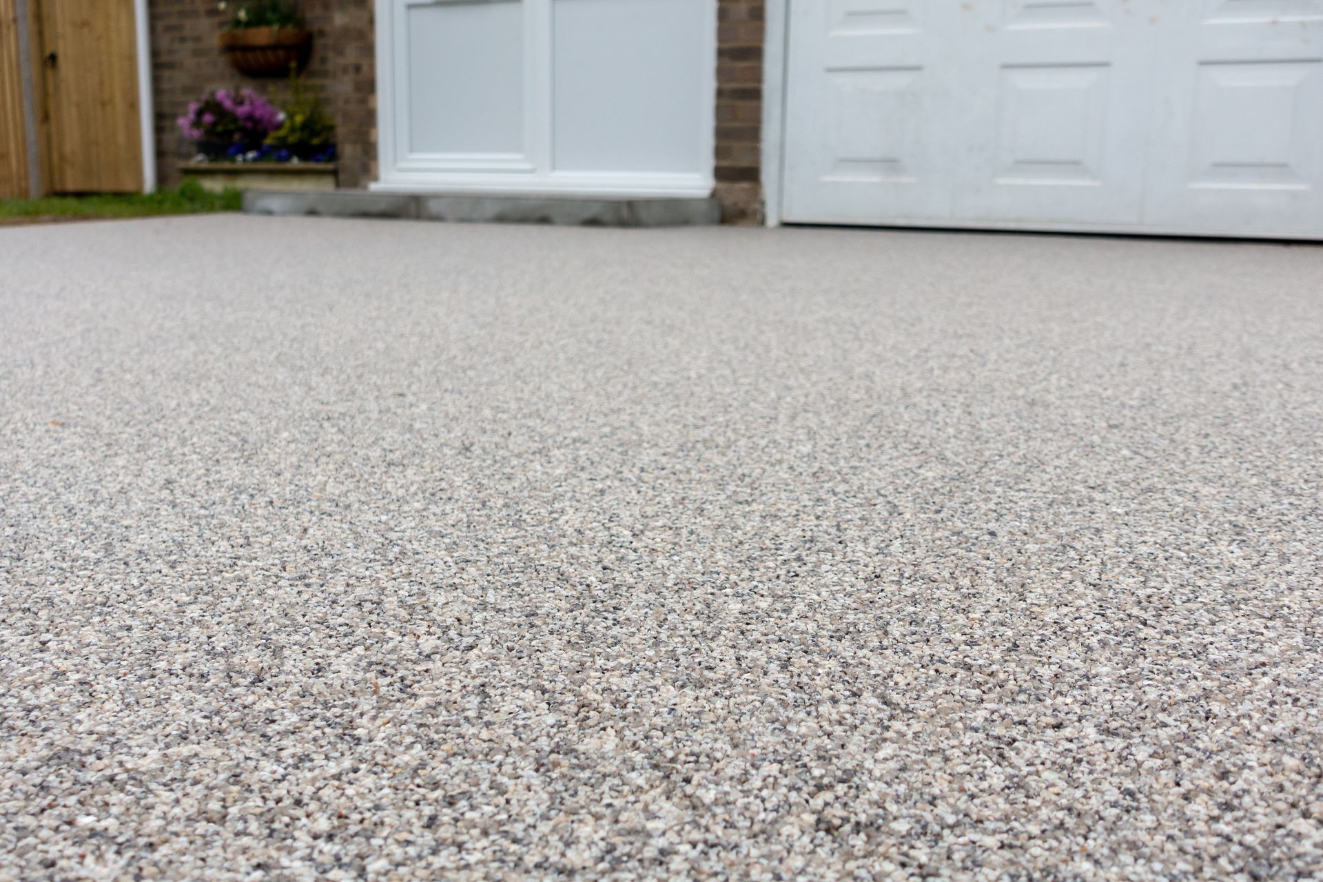 Close-up view of a gravelly, speckled concrete driveway with a white garage door and house entrance in the background.
