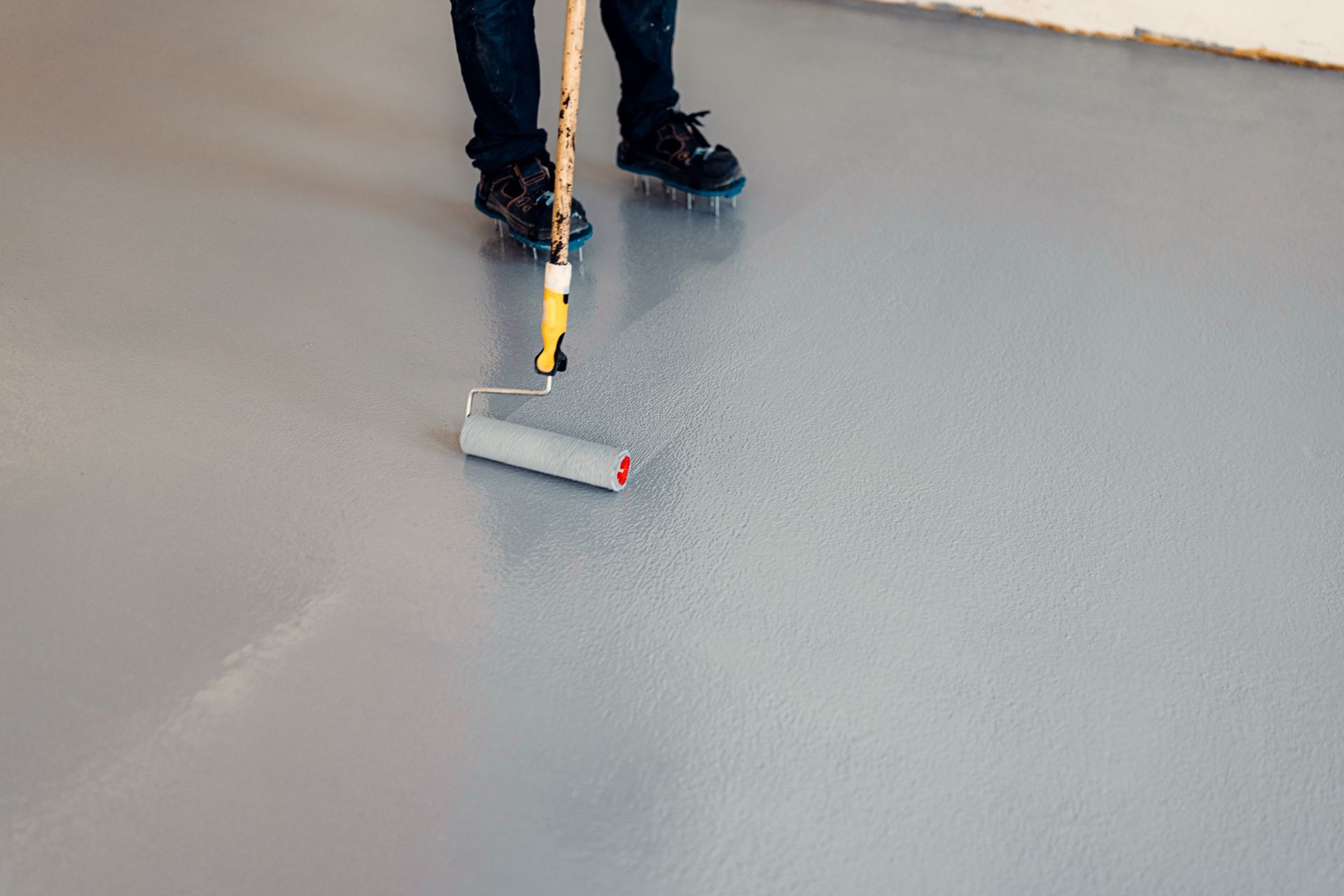 A person is painting a concrete floor with a roller.