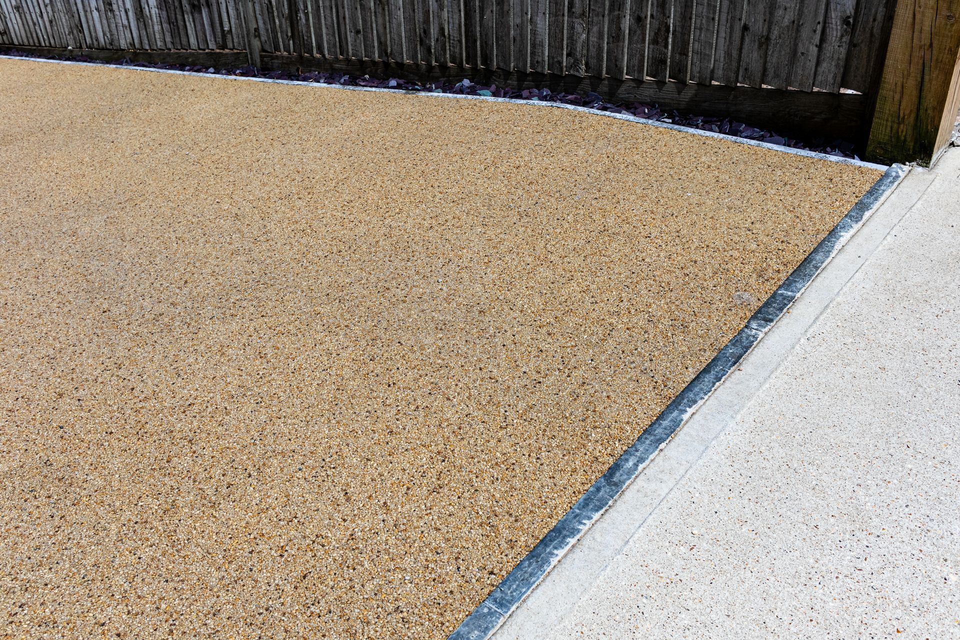 A close up of a gravel driveway with a fence in the background.