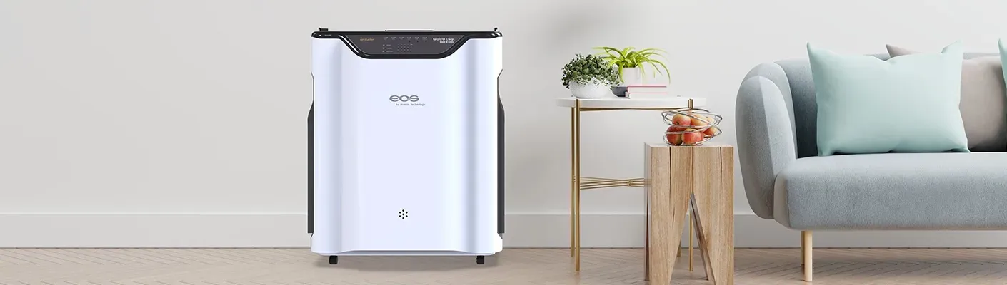 A white air purifier is sitting in a living room next to a couch.