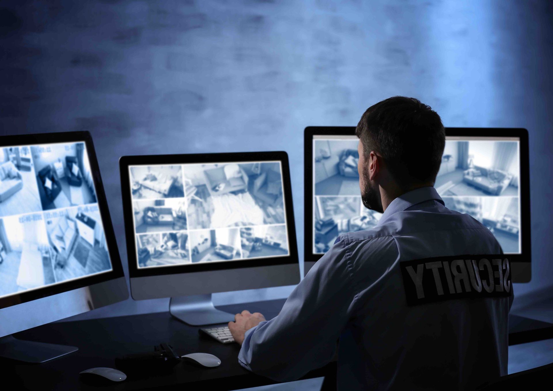 A security guard is sitting in front of three computer monitors.