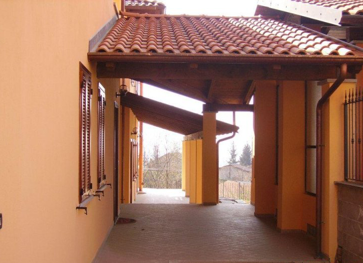 Passaggio coperto con tetto in terracotta, sostenuto da pilastri gialli, che conduce verso una vista in lontananza.