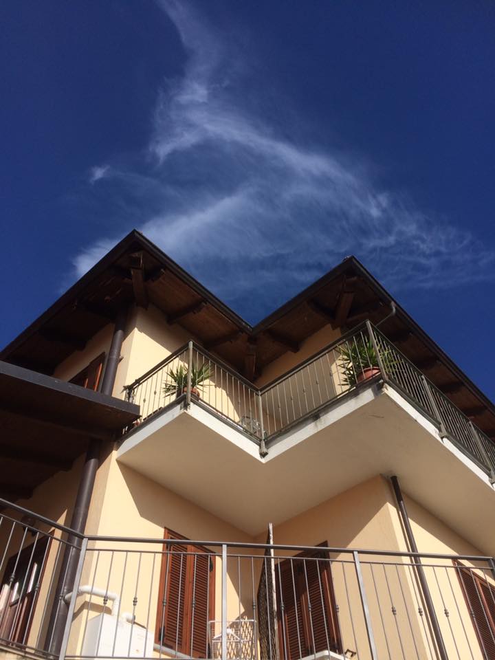 Edificio beige con balconi, persiane marroni e un cielo azzurro con nuvole sottili.