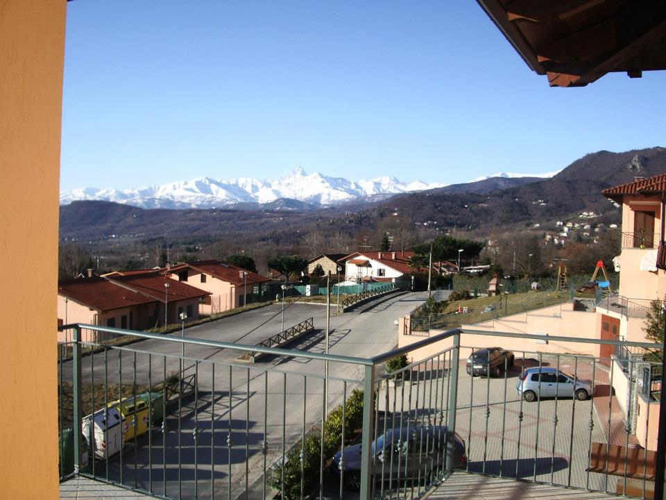 Vista dal balcone che domina una città, una strada e montagne innevate in una giornata di sole.