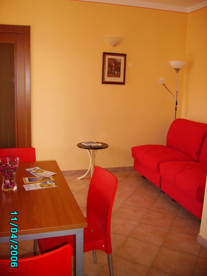 Soggiorno con divano rosso, sedie rosse, tavolo in legno, tavolino rotondo e pareti arancioni.