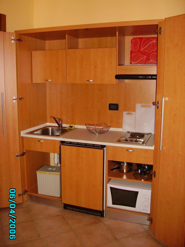 Piccolo angolo cottura con mobili in legno, lavello, piano cottura e forno a microonde.