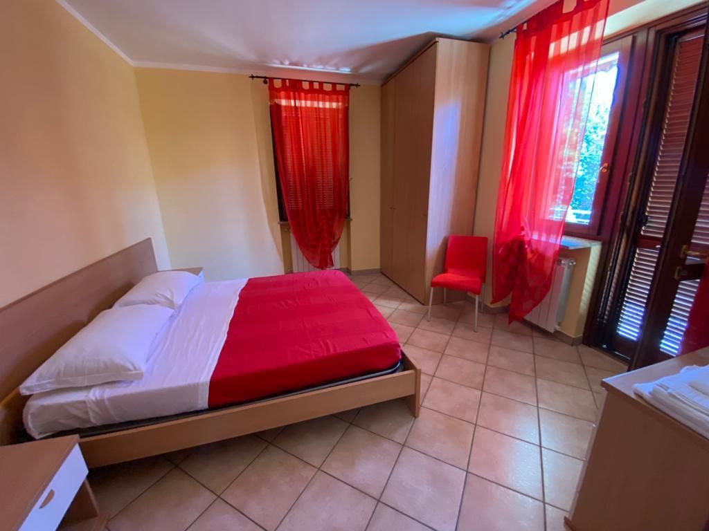 Camera da letto con biancheria da letto e tende rosse, una piccola sedia rossa e una finestra.