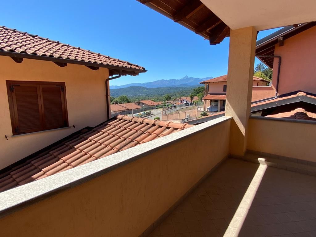 Balcone con tetto in tegole di terracotta, con vista sulle montagne e su altri edifici nelle giornate di sole.