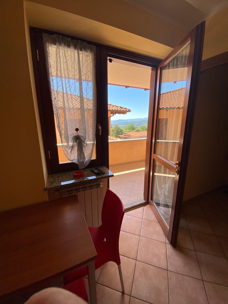 Vista interna di una stanza con porta aperta su un balcone. Giornata luminosa e soleggiata, sedia rossa e vista.