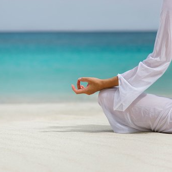 Een vrouw zit in een lotushouding op het strand.