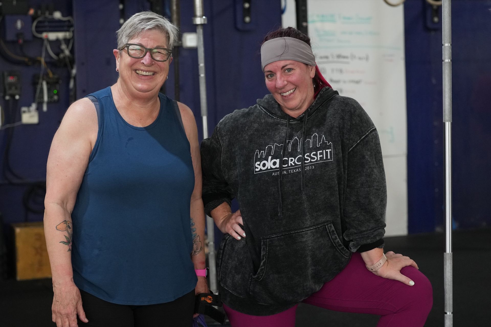 Two women are standing next to each other in a gym and smiling.