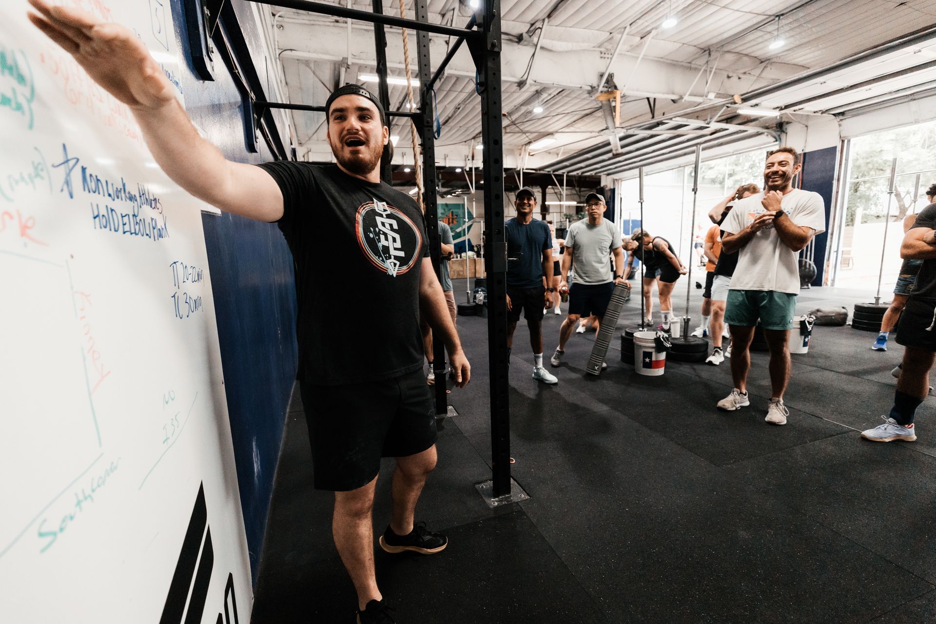 A man is standing in front of a whiteboard in a gym.