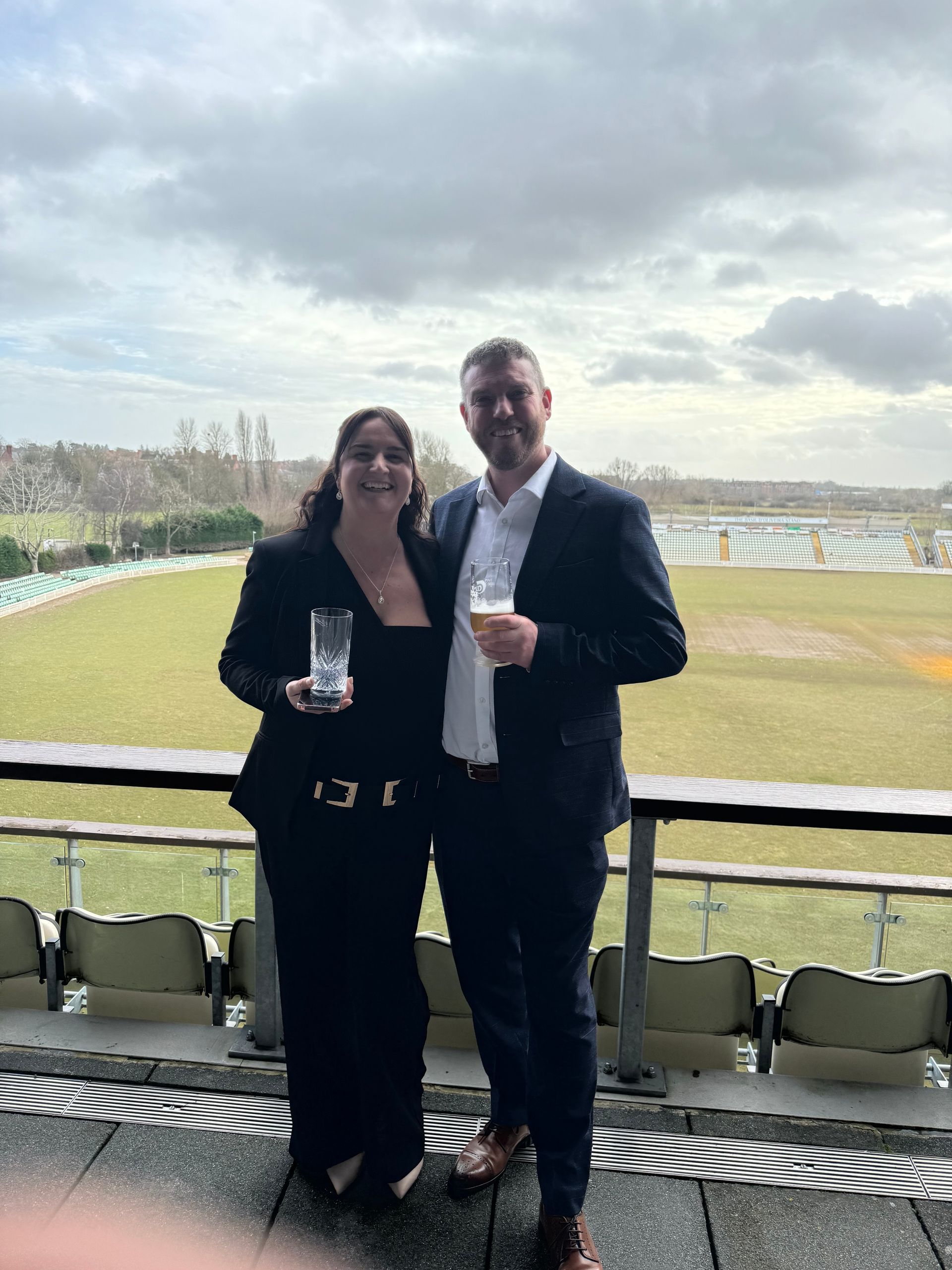 A man and a woman are standing next to each other in front of a field.
